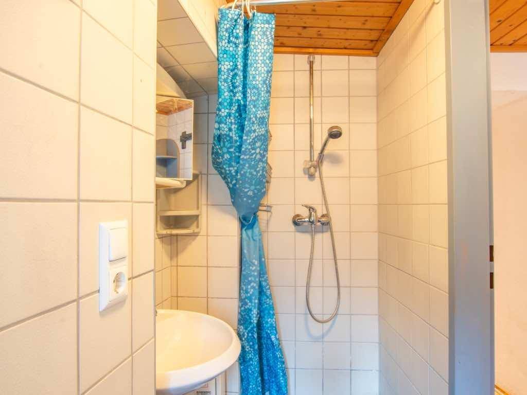 Badezimmer mit weißen Fliesen, Dusche und Waschbecken, ergänzt durch eine Holzdecke.