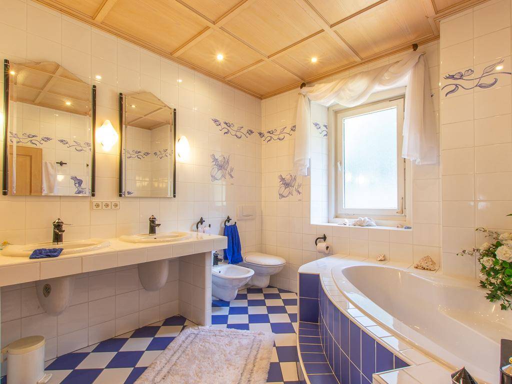 Helles Badezimmer mit Doppelwaschbecken, Eckbadewanne, Bidet und blau-weiß karierten Fliesen.
