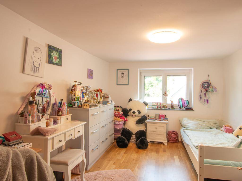 Helles Kinderzimmer mit Holzboden, Schminktisch und großem Fenster mit Blick ins Grüne.