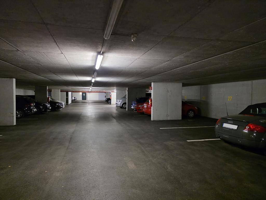 Geräumige Tiefgarage mit zahlreichen Stellplätzen und Betonwänden unter künstlicher Beleuchtung.