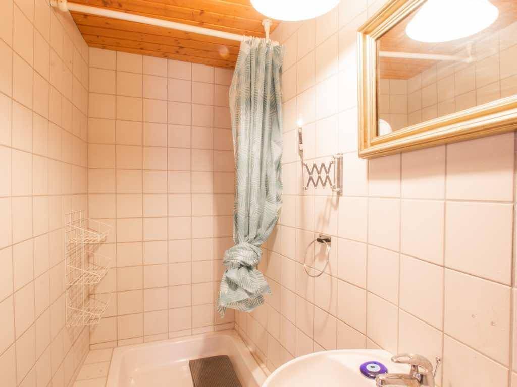Kleines Badezimmer mit weißen Fliesen, Duschvorhang und Waschbecken unter einer Holzdecke.