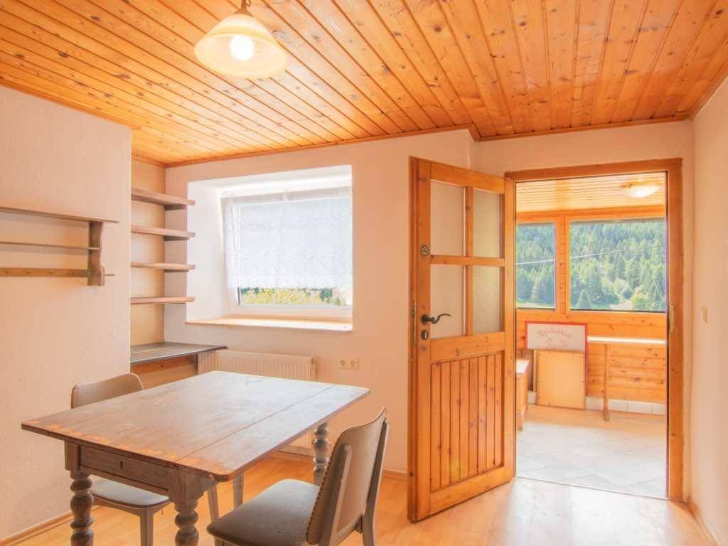 Essbereich mit Holztisch, Stühlen und einer Holzdecke, angrenzend an einen Raum mit Bergblick.