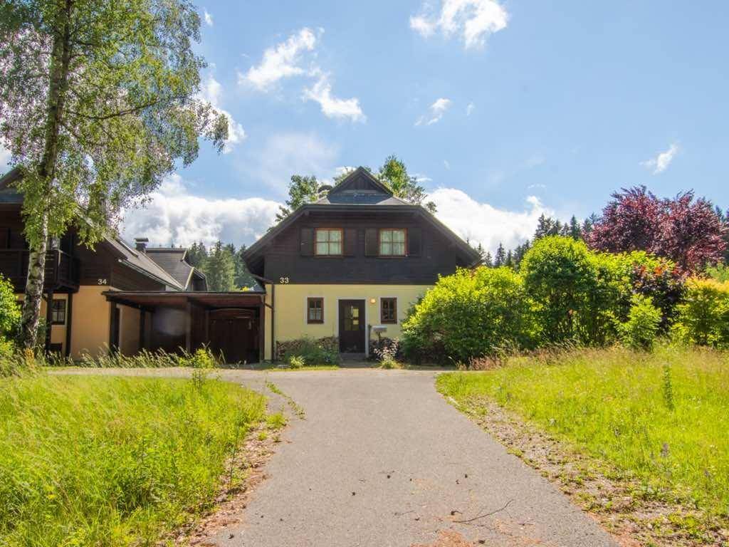 Freistehendes Haus mit gelber Fassade und dunklem Dach, umgeben von üppiger Natur und Wiesen.