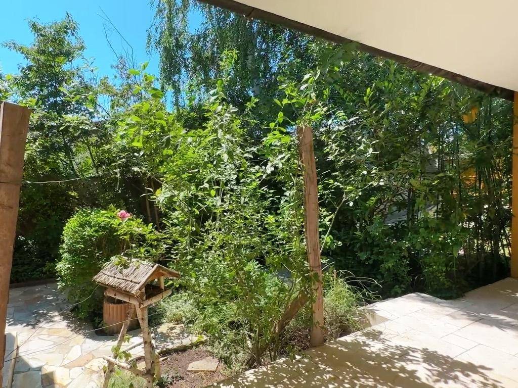 Grüner Gartenbereich mit Bäumen und Sträuchern, der viel Schatten spendet.