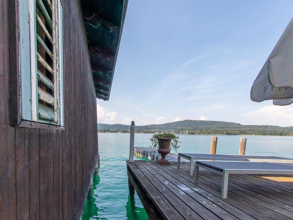 Holzterrasse am See mit Sonnenliegen, Sonnenschirm und weitem Blick auf die umliegende Natur.
