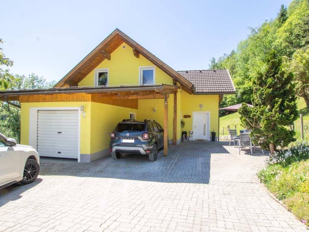 Gelbes Haus mit Garage und Carport, gepflasterter Einfahrt und Sitzbereich im Freien.