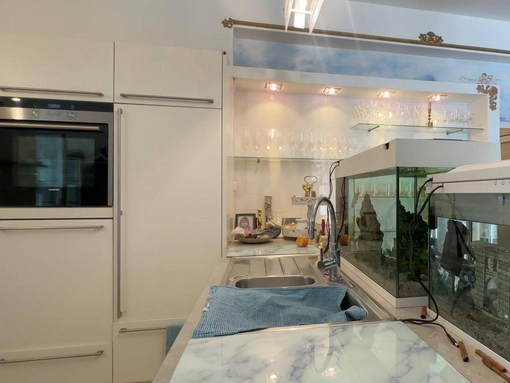 Moderne weiße Einbauküche mit Spülbecken, Marmor-Arbeitsplatte und integriertem Aquarium.