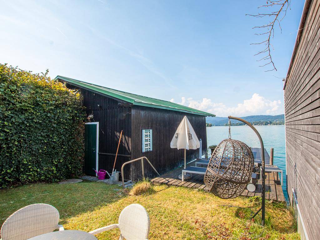 Idyllischer Gartenbereich am See mit Schaukelstuhl und weitem Blick auf das Wasser und die Berge.