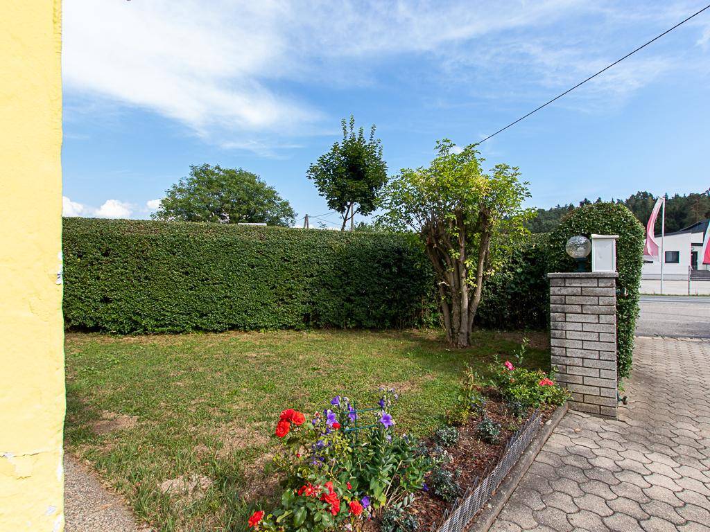 Kleiner Vorgarten mit Rasenfläche, Blumenbeeten und einer gepflegten Hecke.