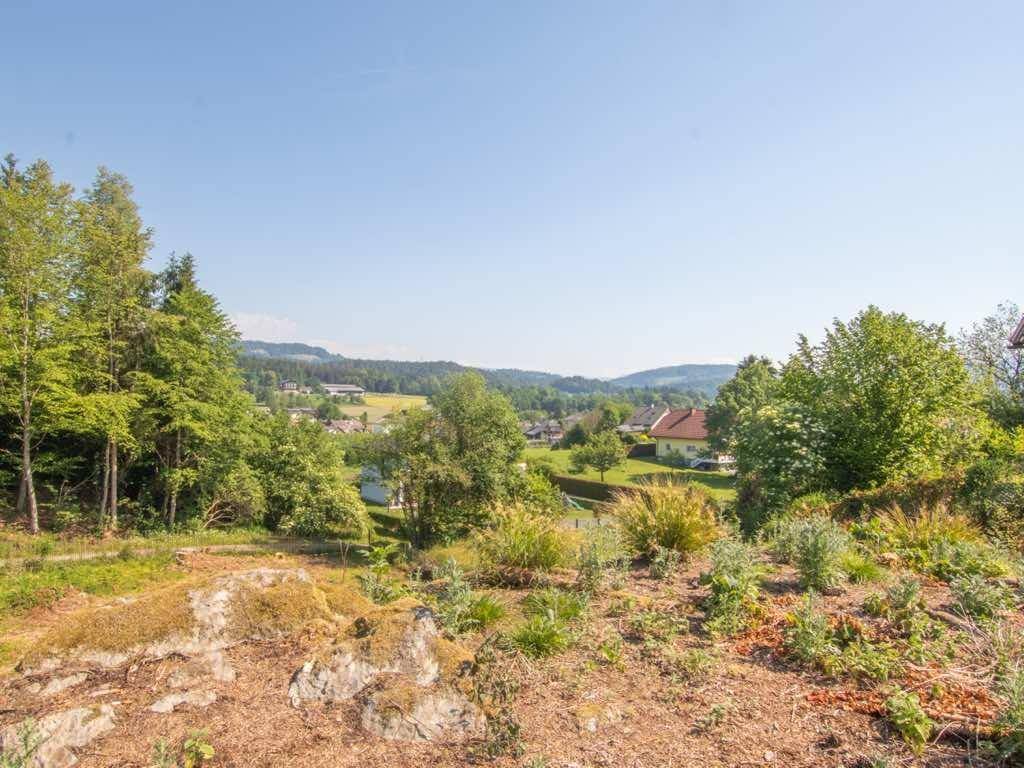Blick über eine karge Fläche auf eine grüne Talandschaft mit Häusern in der Ferne.