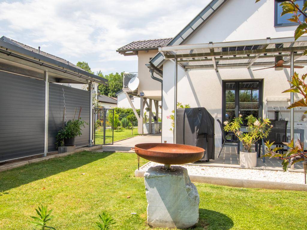 Seitenansicht des Hauses mit überdachter Terrasse, Garten und dekorativer Feuerschale.