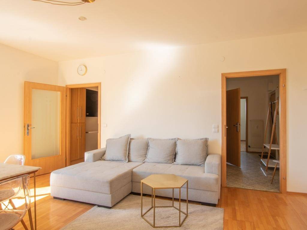 Gemütliches Wohnzimmer mit hellem Sofa, Holzboden und Zugang zu weiteren Räumen.