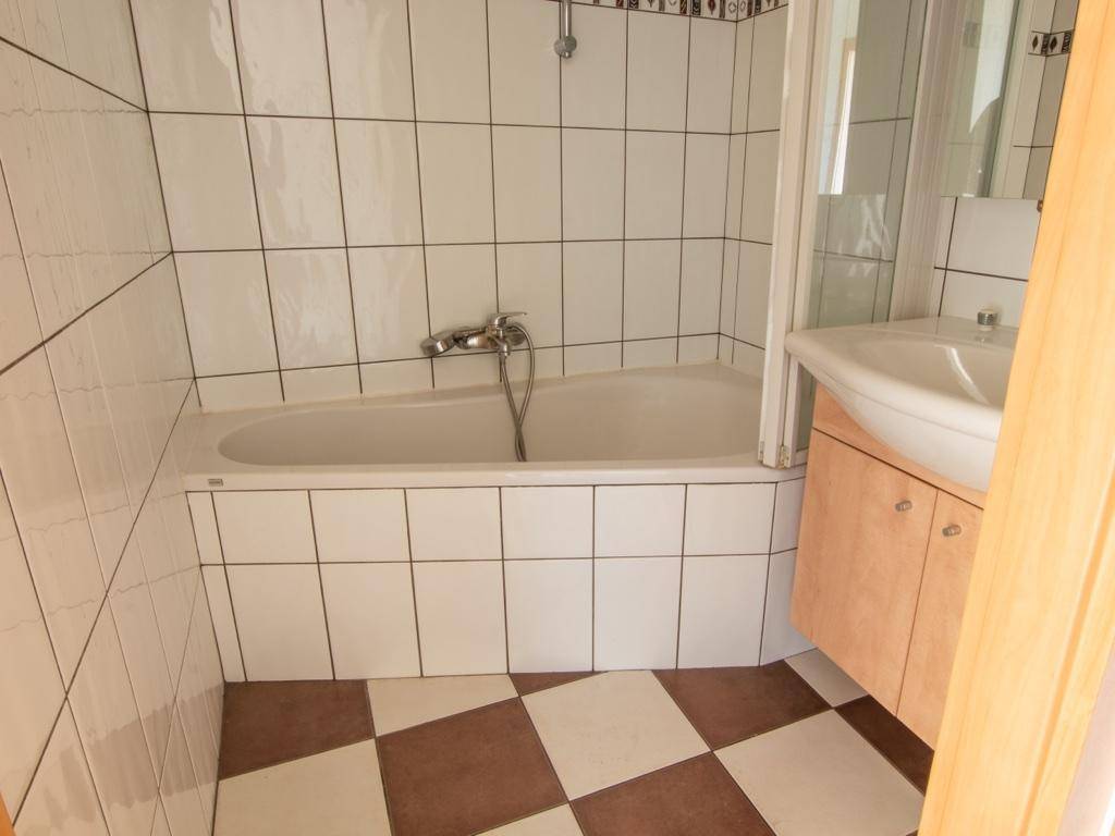 Badezimmer mit Badewanne, Waschbecken und weiß-braun kariertem Fliesenboden.