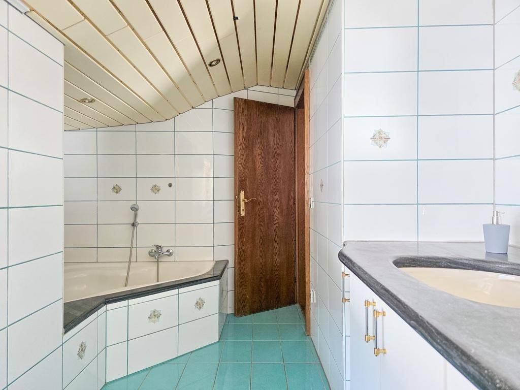 Badezimmer mit Eckbadewanne, weißen Fliesen und Holzdecke im Dachgeschoss.