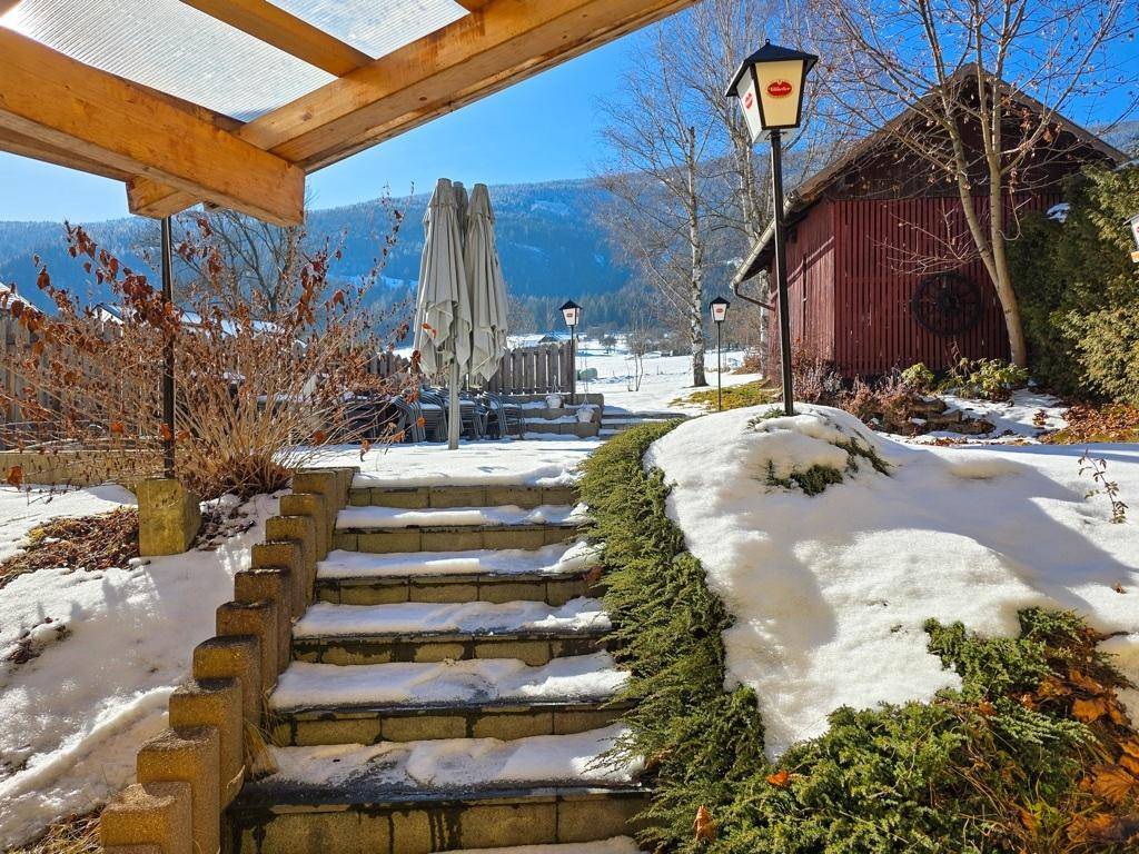 Schneebedeckter Gartenbereich mit Steintreppe, Sonnenschirmen und Blick auf die Berge.