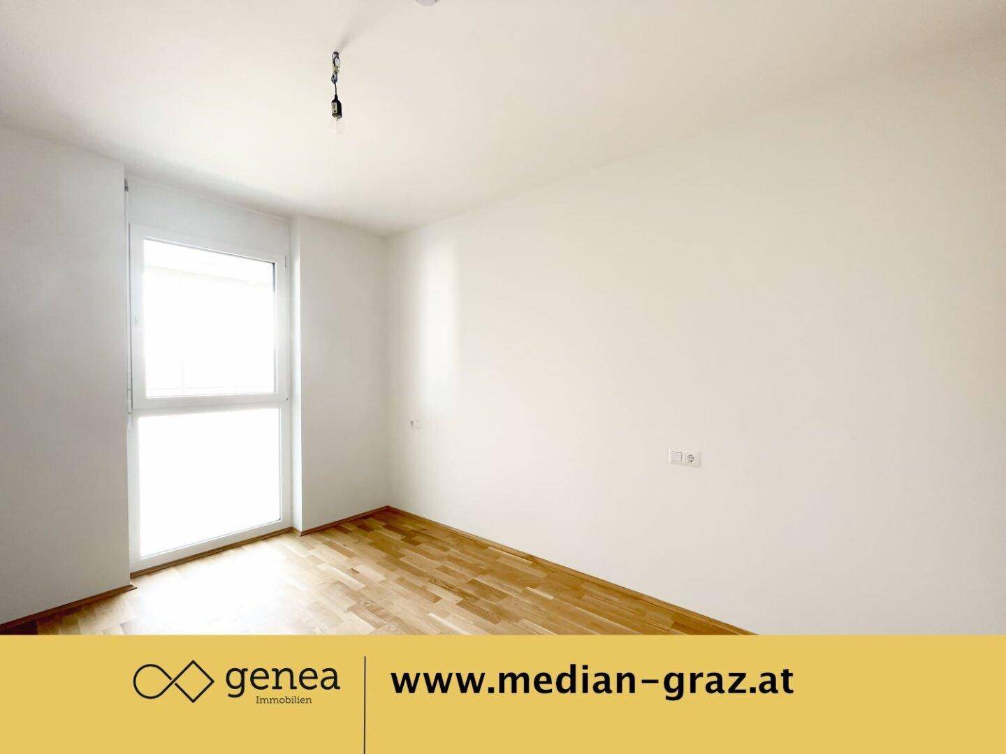 Leeres Zimmer mit hellem Parkettboden und großem Fenster, das viel Tageslicht hereinlässt.