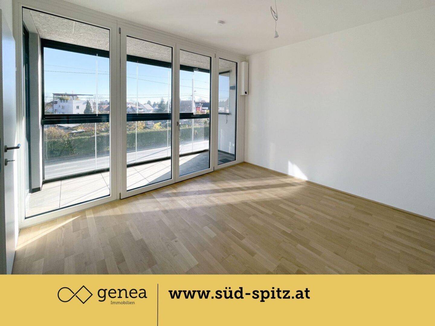 Heller Wohnraum mit Parkettboden und einer Fensterfront, die viel Licht hereinlässt.