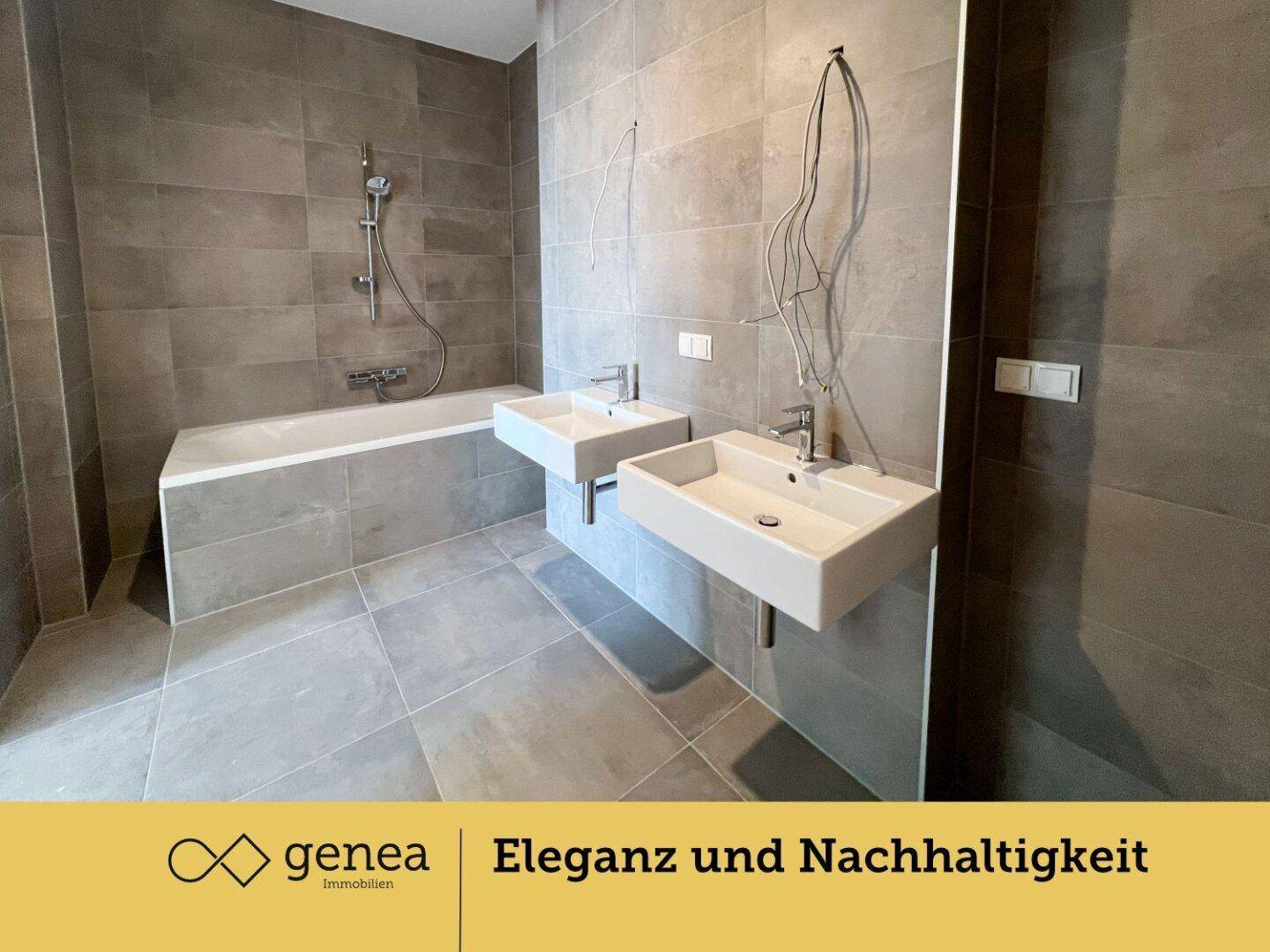 Geräumiges Badezimmer mit zwei Waschbecken, Badewanne und modernen grauen Fliesen.