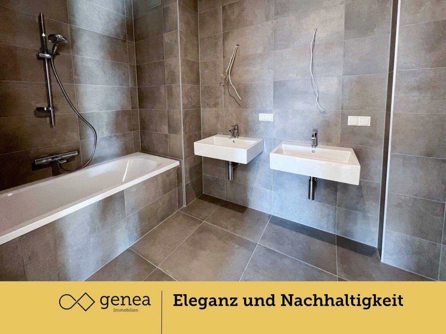 Modernes Badezimmer mit grauen Fliesen, Badewanne und zwei Waschbecken.