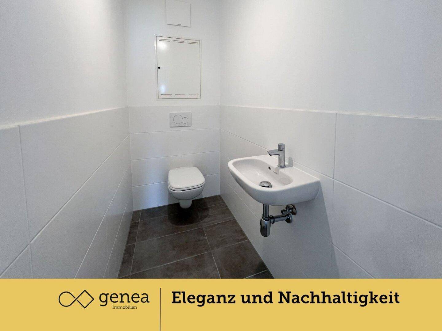 Separates WC mit Wand-WC, kleinem Waschbecken und weißen Fliesen an den Wänden.