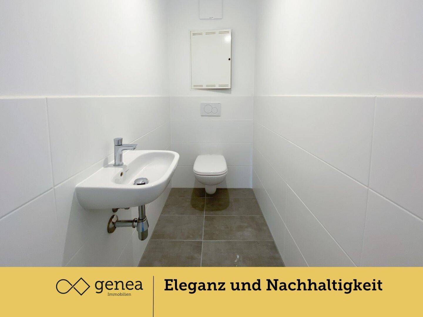 Separates WC mit modernen weißen Fliesen, wandhängender Toilette und kleinem Handwaschbecken.