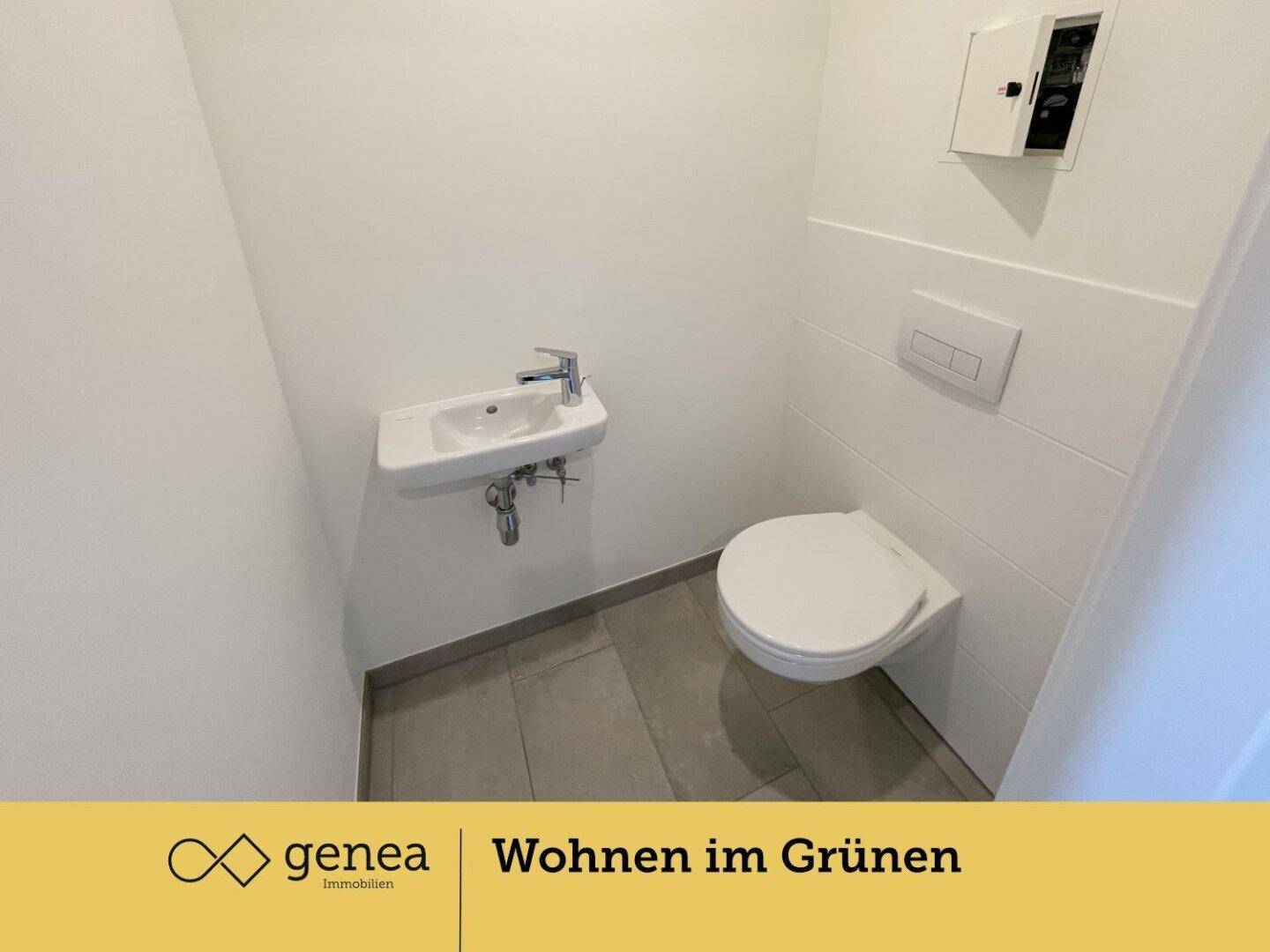 Modernes Gäste-WC mit wandhängendem WC, kleinem Waschbecken und hellen Fliesen an Wänden und Boden.
