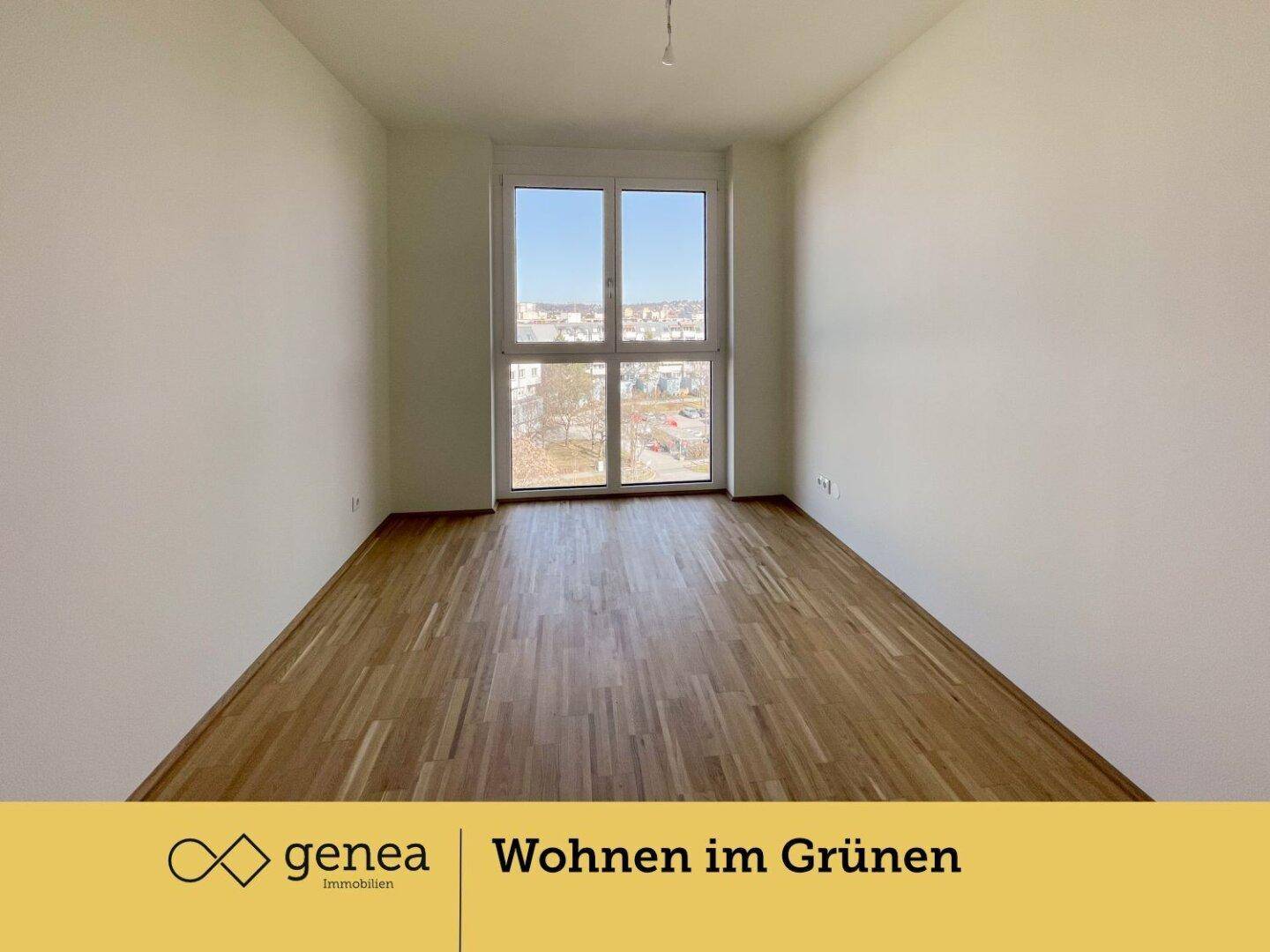 Leeres Schlafzimmer mit Parkettboden und einem großen Fenster, das viel Tageslicht hereinlässt.