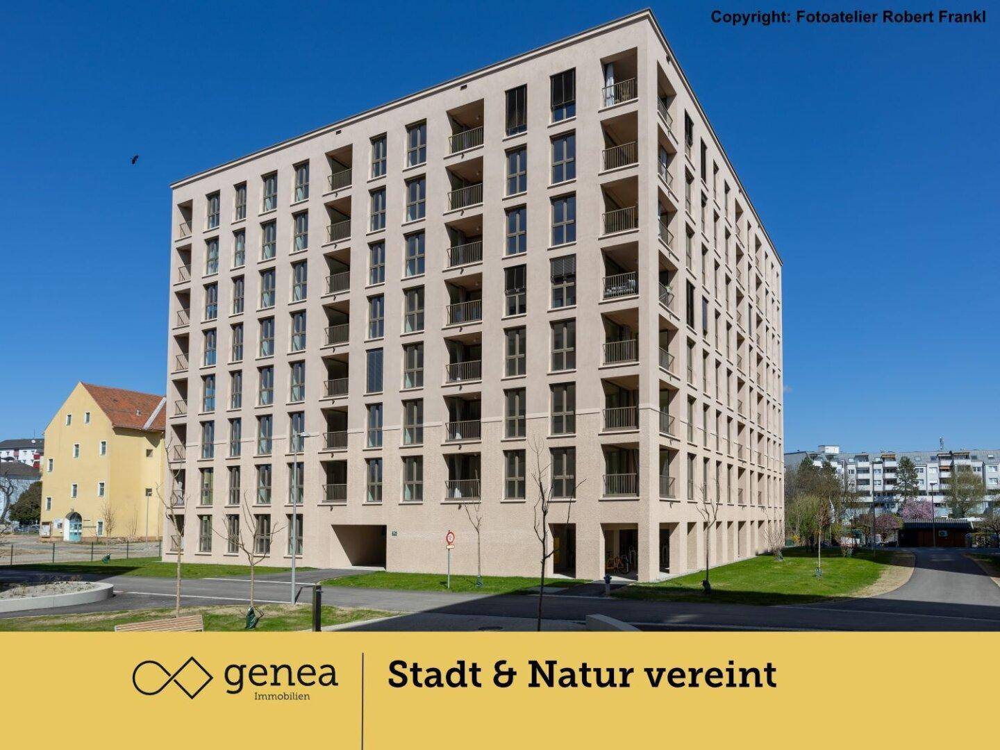 Modernes Mehrfamilienhaus mit beiger Fassade und zahlreichen Balkonen unter blauem Himmel.