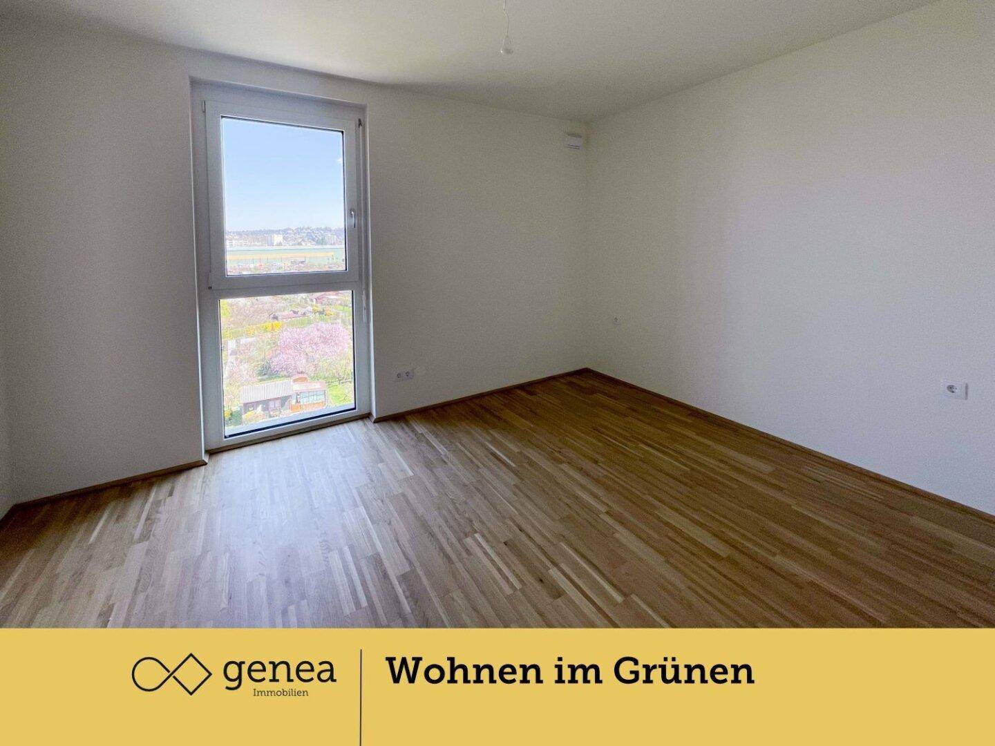Helles Schlafzimmer mit Parkettboden und großem Fenster, das einen Blick ins Grüne bietet.