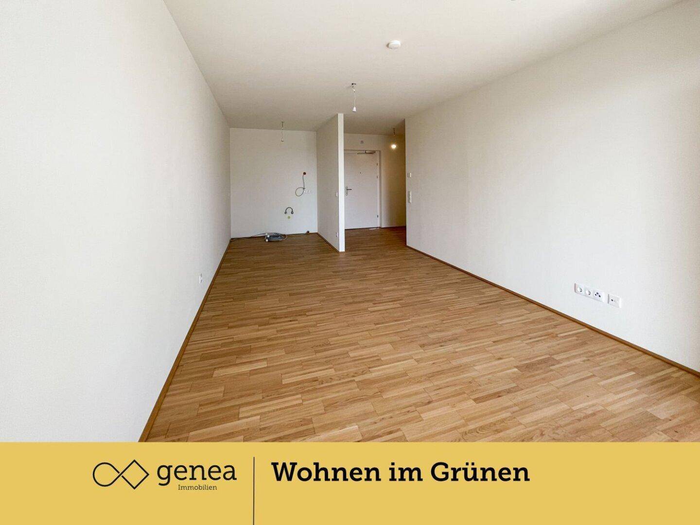 Offener Wohnbereich mit Holzparkettboden und vorbereiteten Anschlüssen für eine Küche.