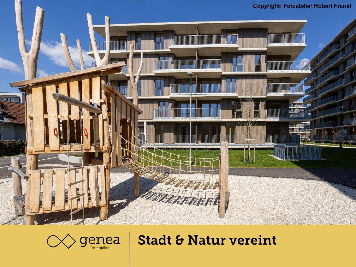 Holzklettergerüst auf einem Spielplatz vor modernen Wohngebäuden mit Balkonen.