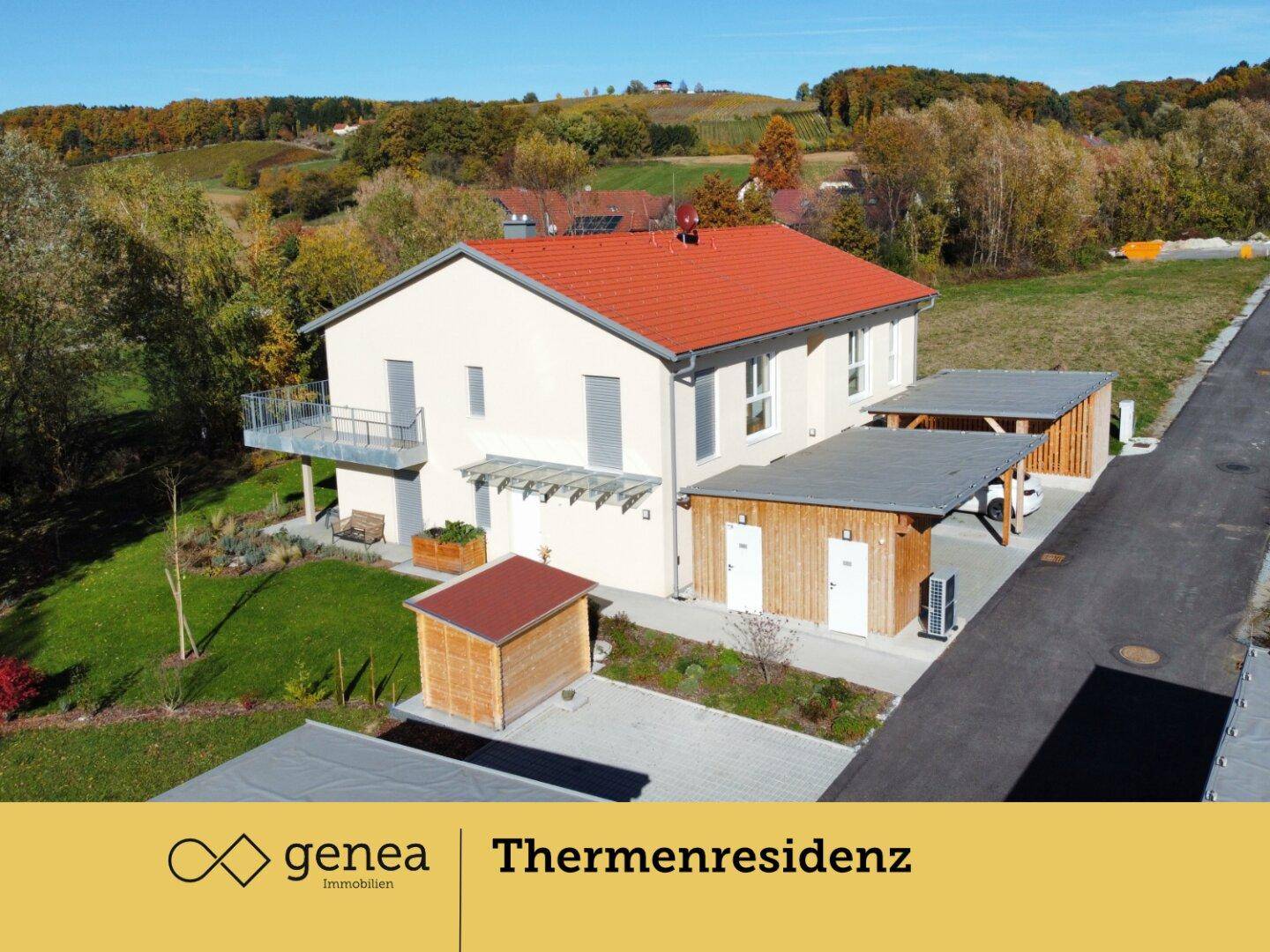 Luftaufnahme eines modernen Hauses mit rotem Dach, Carports und weitläufiger Landschaft im Hintergrund.