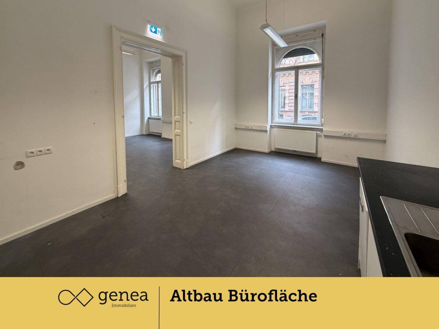Offener Büroraum mit Küchenzeile und großen Fenstern, die eine helle Arbeitsumgebung schaffen.