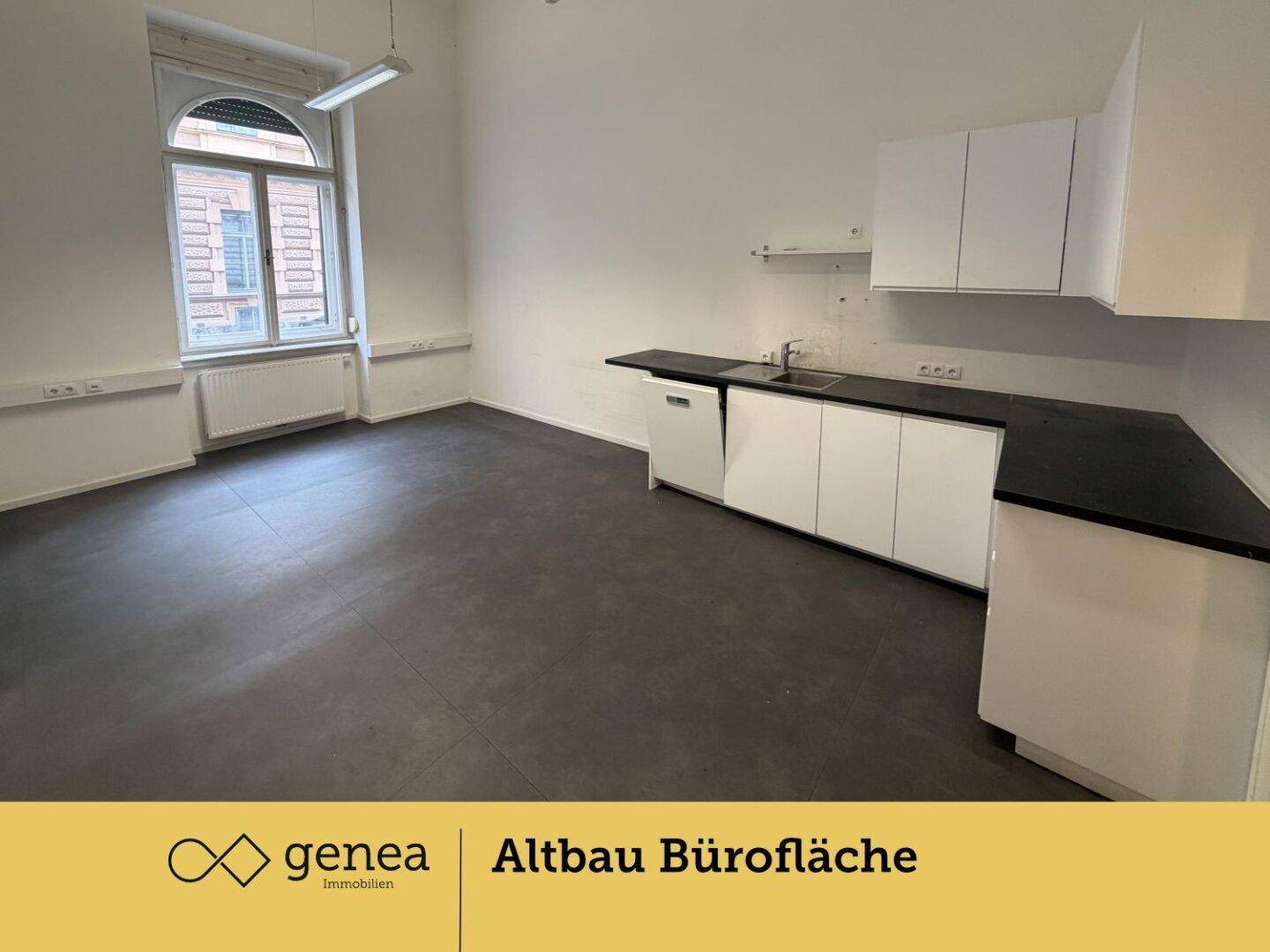 Bürofläche mit funktionaler Küchenzeile, dunklem Boden und Blick auf die Fenster.