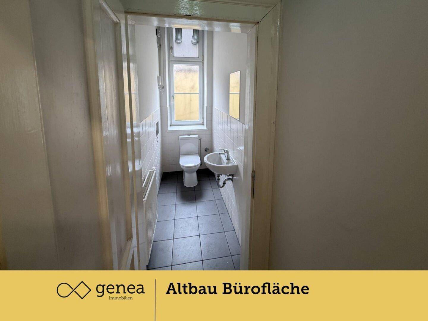 Kleiner Toilettenraum mit Fenster, WC und Waschbecken, gefliest in Weiß und Dunkelgrau.