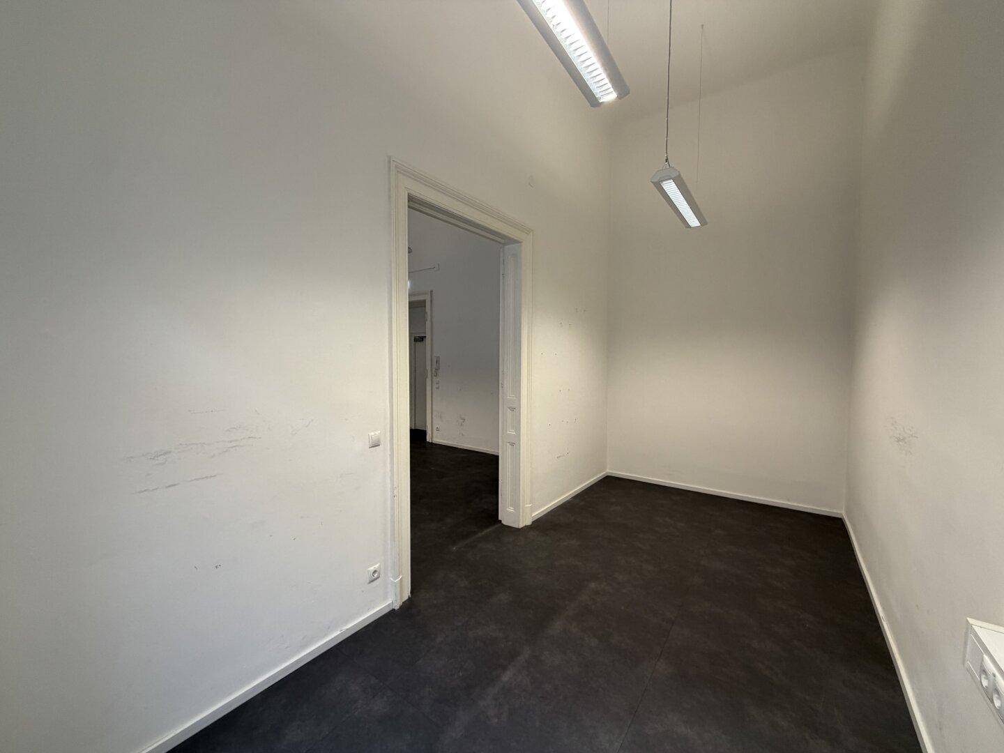 Leerer Büroraum mit modernen Deckenleuchten und dunklem Bodenbelag.