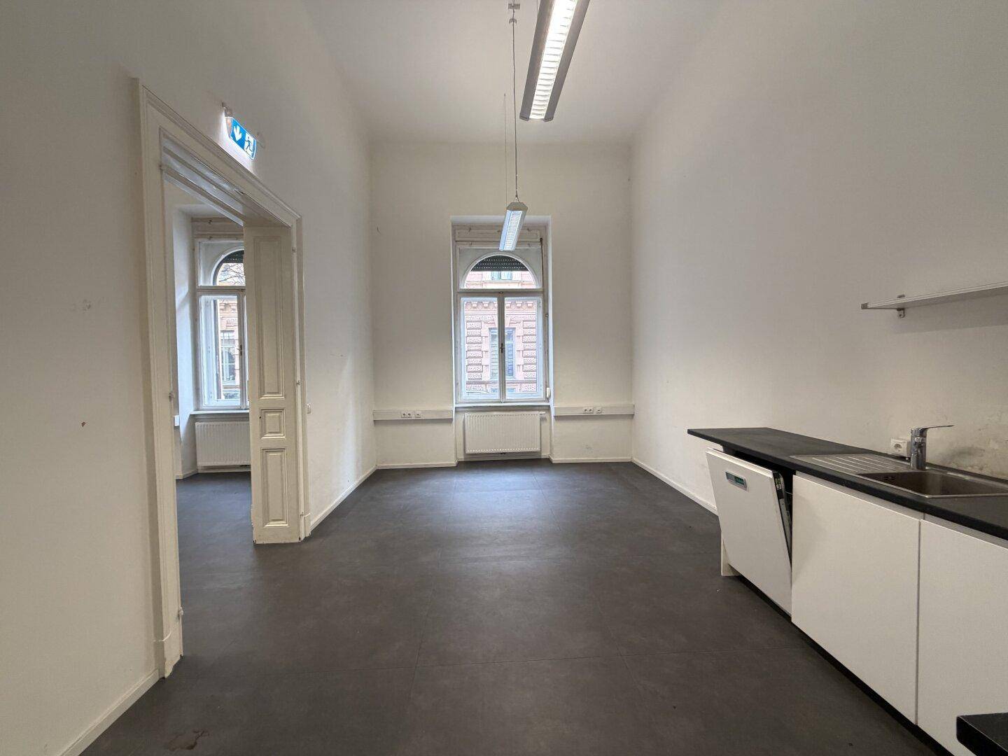 Büroraum mit integrierter Küchenzeile und Blick durch ein großes Fenster.