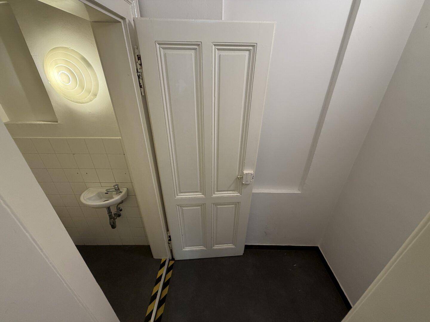 Kleiner Raum mit Waschbecken und schmaler Tür, möglicherweise ein Gäste-WC.