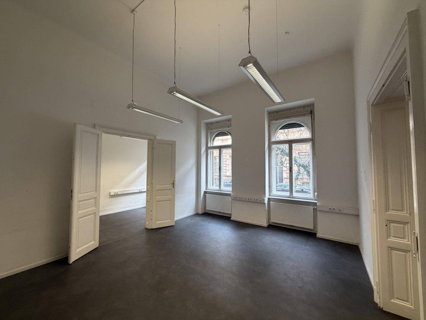 Großes Büro mit hohen Decken, mehreren Fenstern und dunklem Bodenbelag.