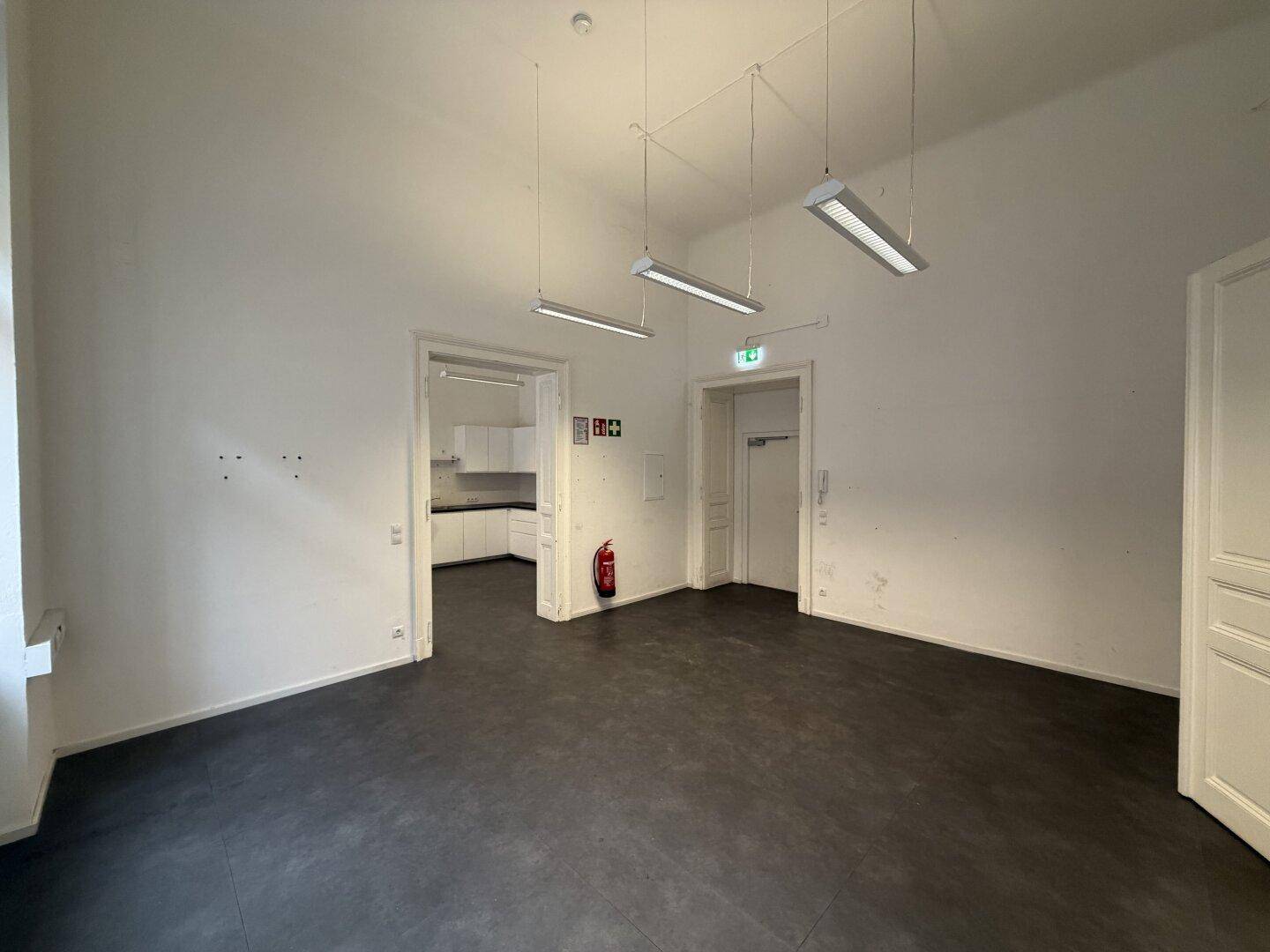 Geräumiges Büro mit dunklem Boden, weißen Wänden und einem Feuerlöscher.