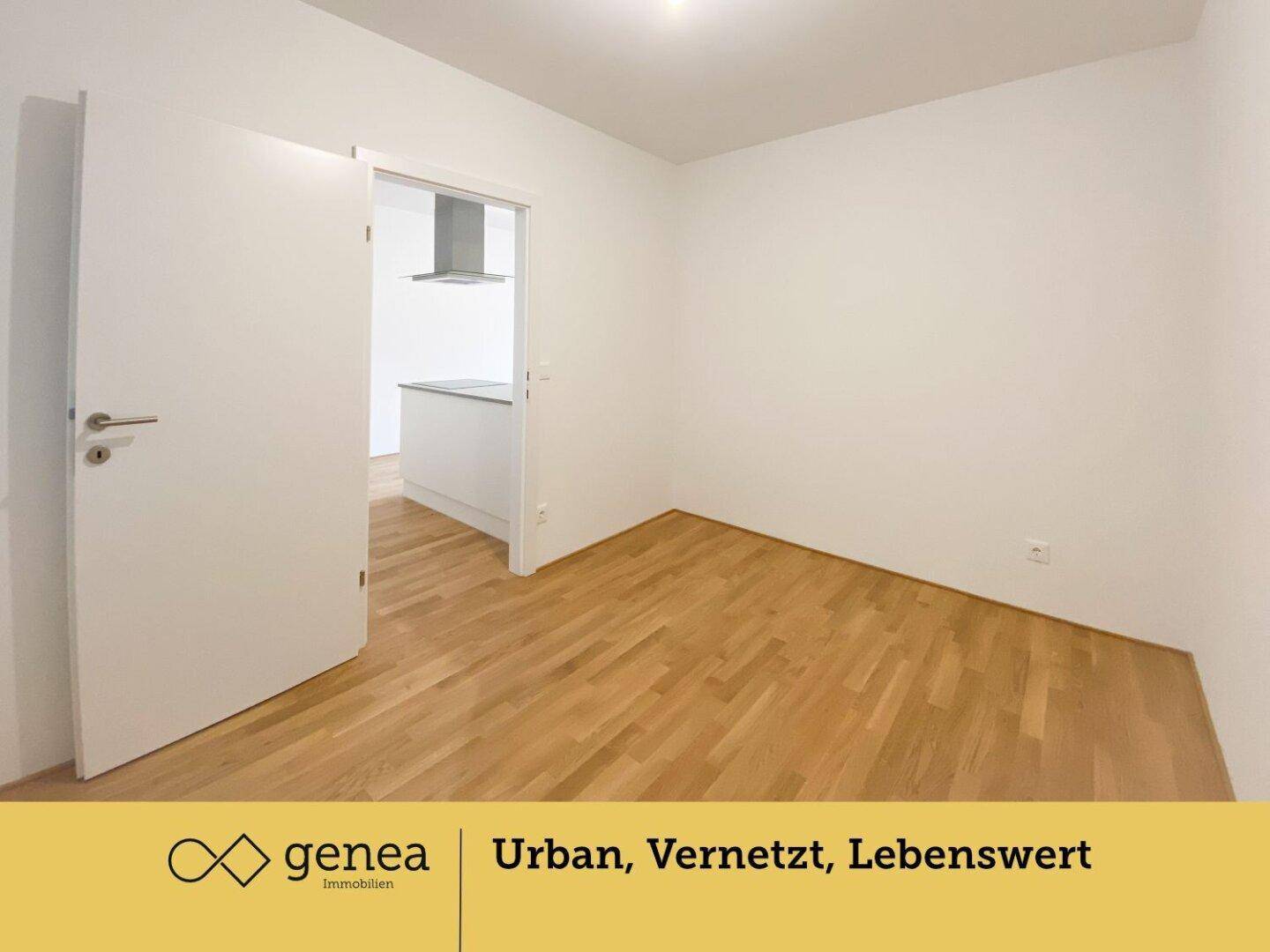 Leeres Zimmer mit hellem Parkettboden und weiß gestrichenen Wänden, Blick in die Küche.