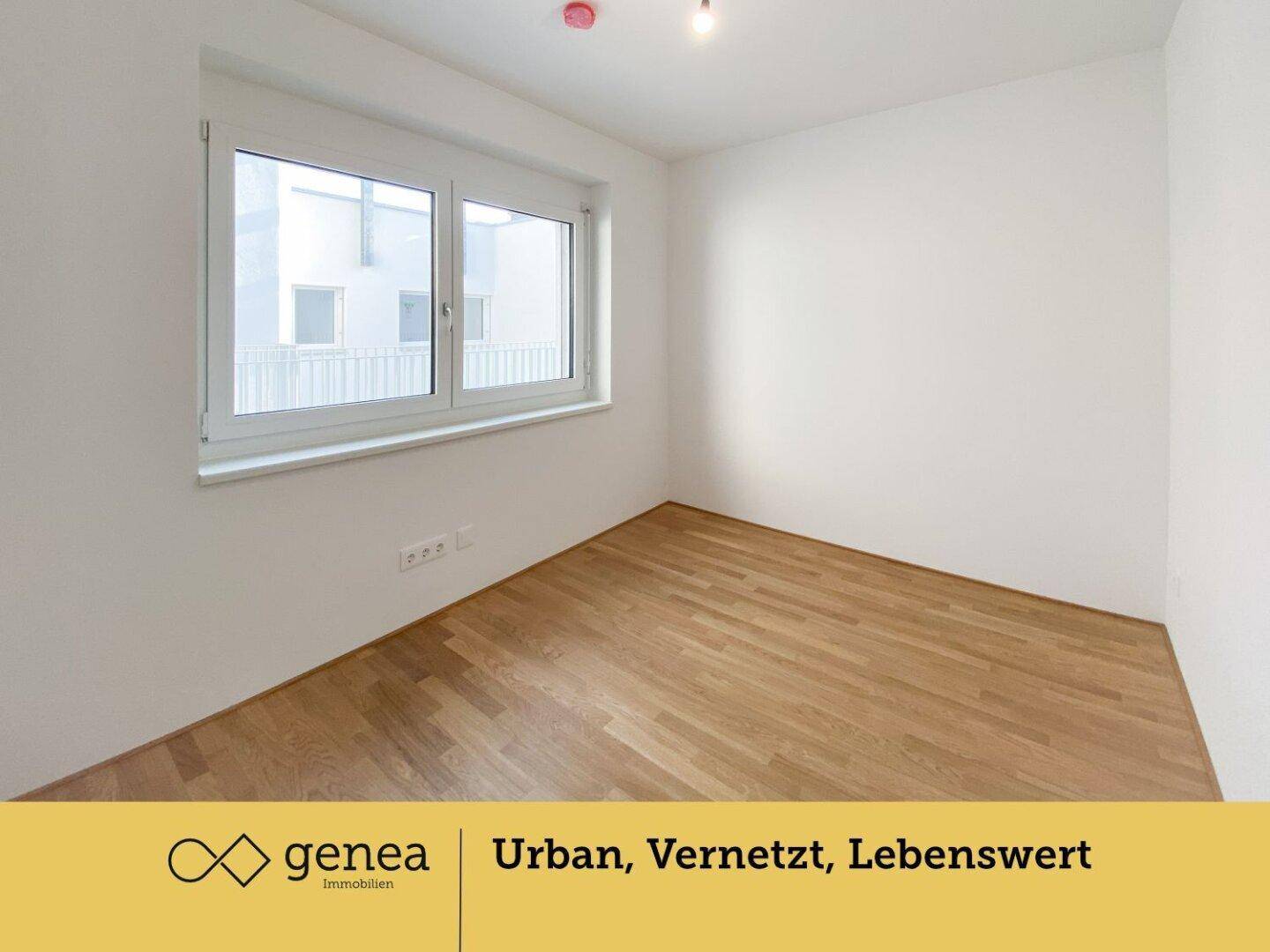 Leeres Schlafzimmer mit hellem Parkettboden und einem großen Fenster, das den Raum erhellt.