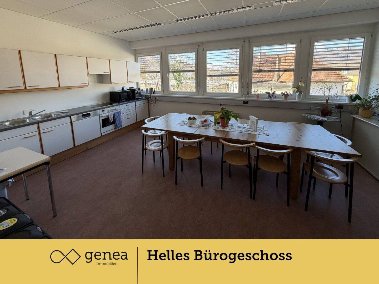 Große Gemeinschaftsküche mit weißen Schränken, Spülmaschine und einem langen Holztisch für Besprechungen oder Pausen.