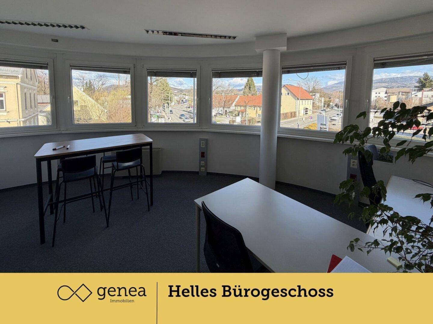 Helles Büro mit Teppichboden, Stehtischen und großen Fenstern, die einen weiten Blick auf die Umgebung ermöglichen.