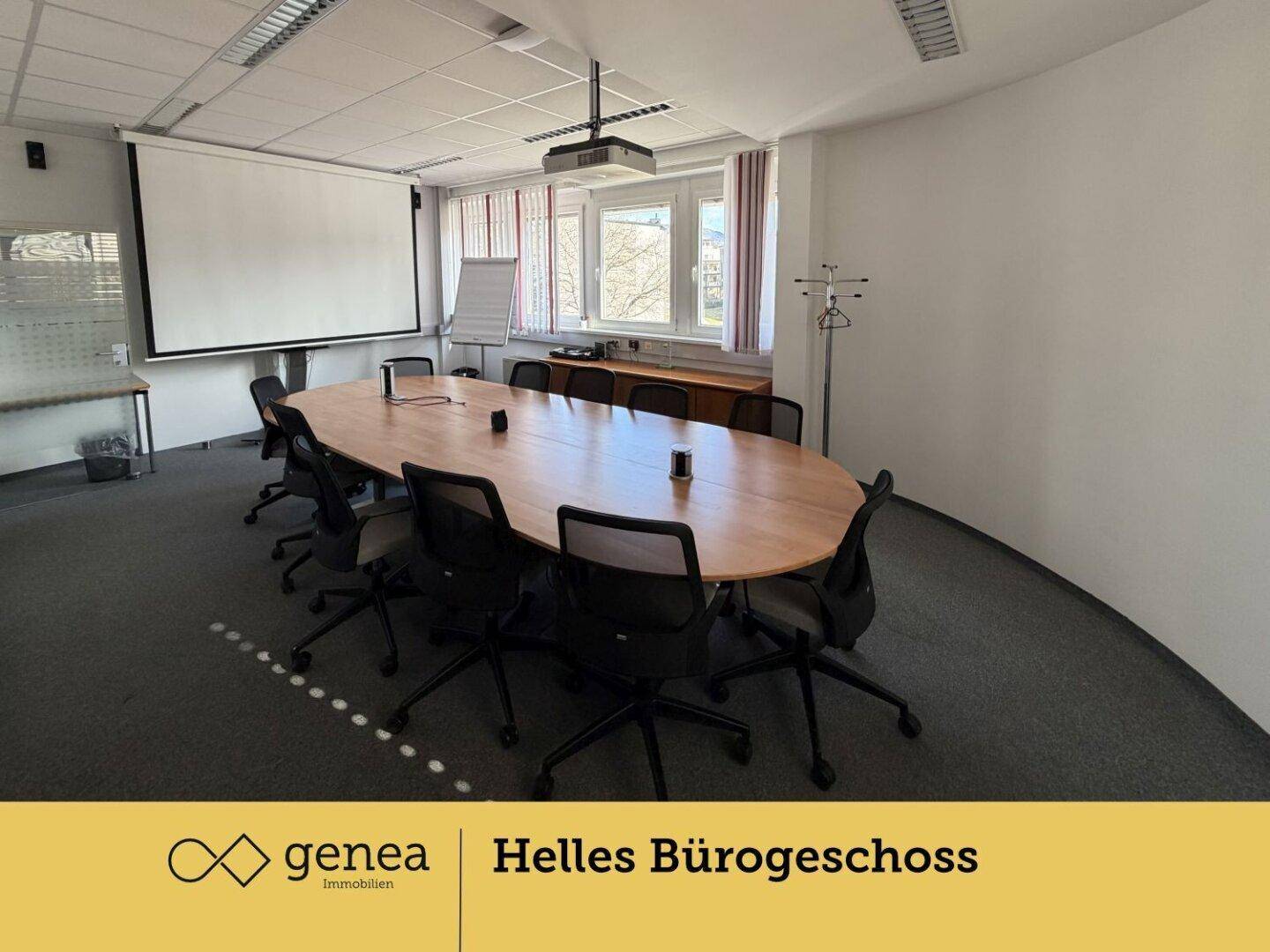 Großer Konferenzraum mit ovalem Holztisch, vielen Stühlen und einem Beamer für Präsentationen.