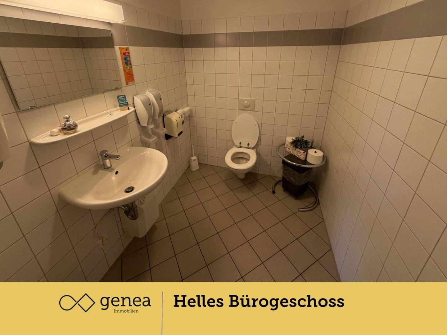 Helles Badezimmer mit Fliesenboden, Waschbecken und Toilette, ausgestattet mit einem Spiegel und Handtuchspender.