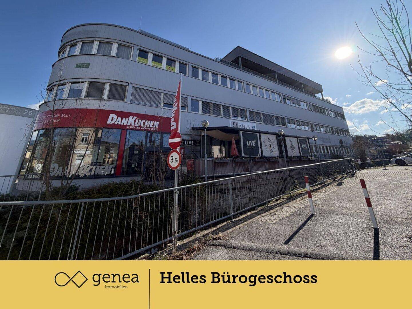 Ansicht des Geschäftsgebäudes von der Straße, zeigt die Fassade mit mehreren Etagen und umliegende Parkplätze.
