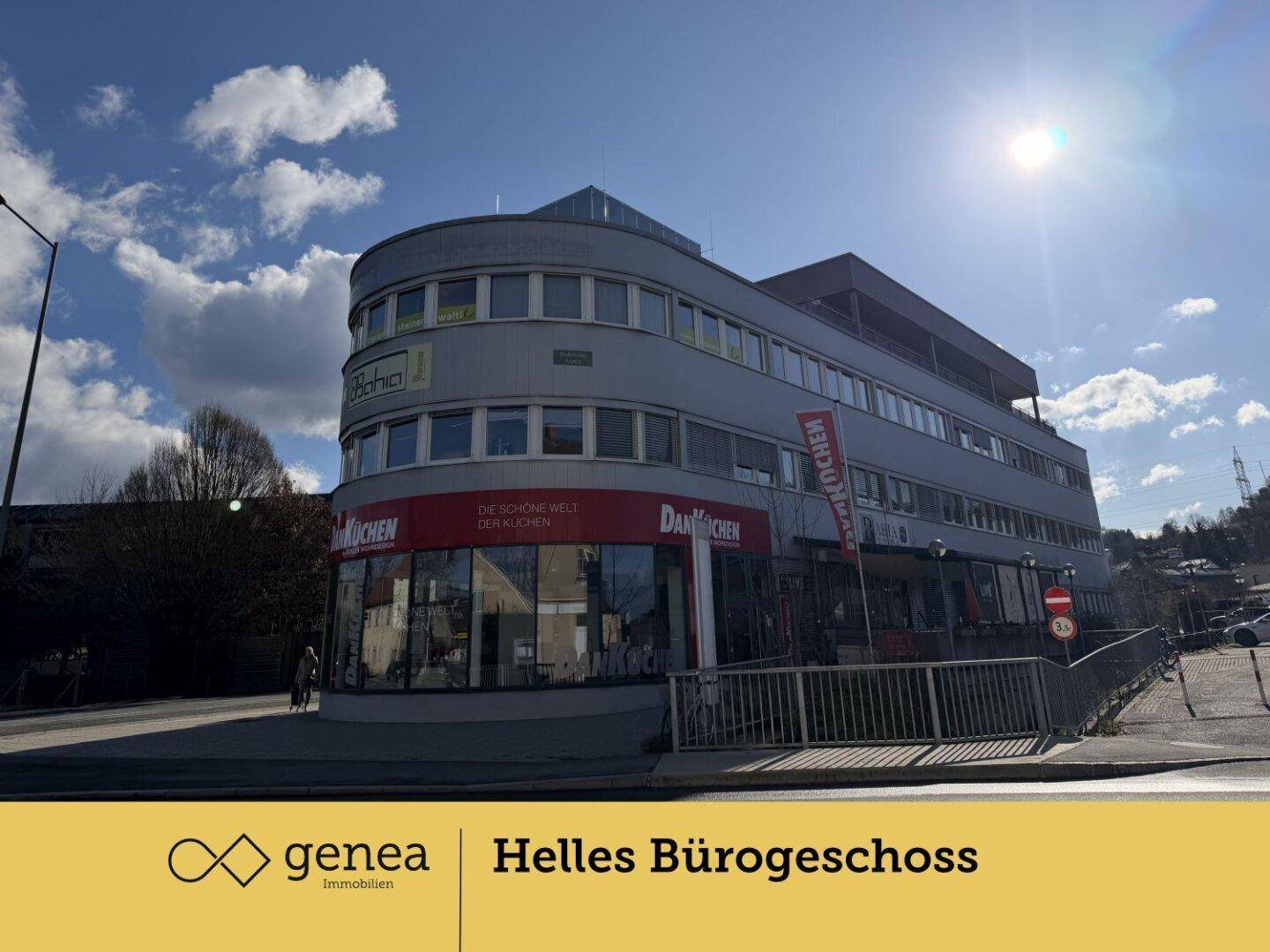 Gesamtansicht des modernen Bürogebäudes mit runder Ecke und großen Fenstern unter blauem Himmel.