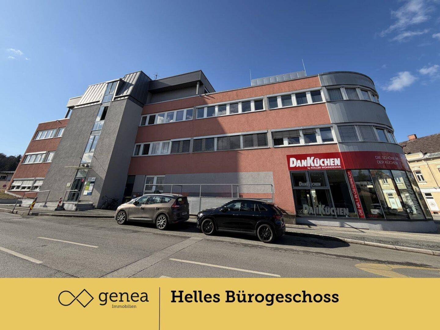 Seitenansicht des Geschäftsgebäudes mit roter Fassade und großen Fensterfronten, geparkte Autos davor.