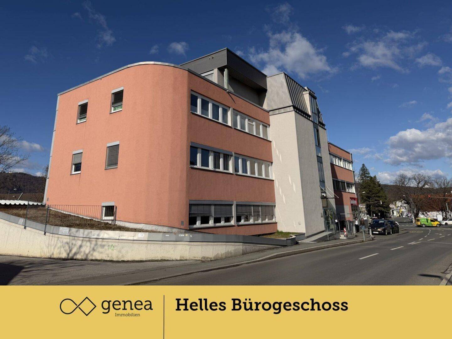 Weitwinkelaufnahme des Geschäftsgebäudes mit roter Fassade und vielen Fenstern, umgeben von Bäumen.